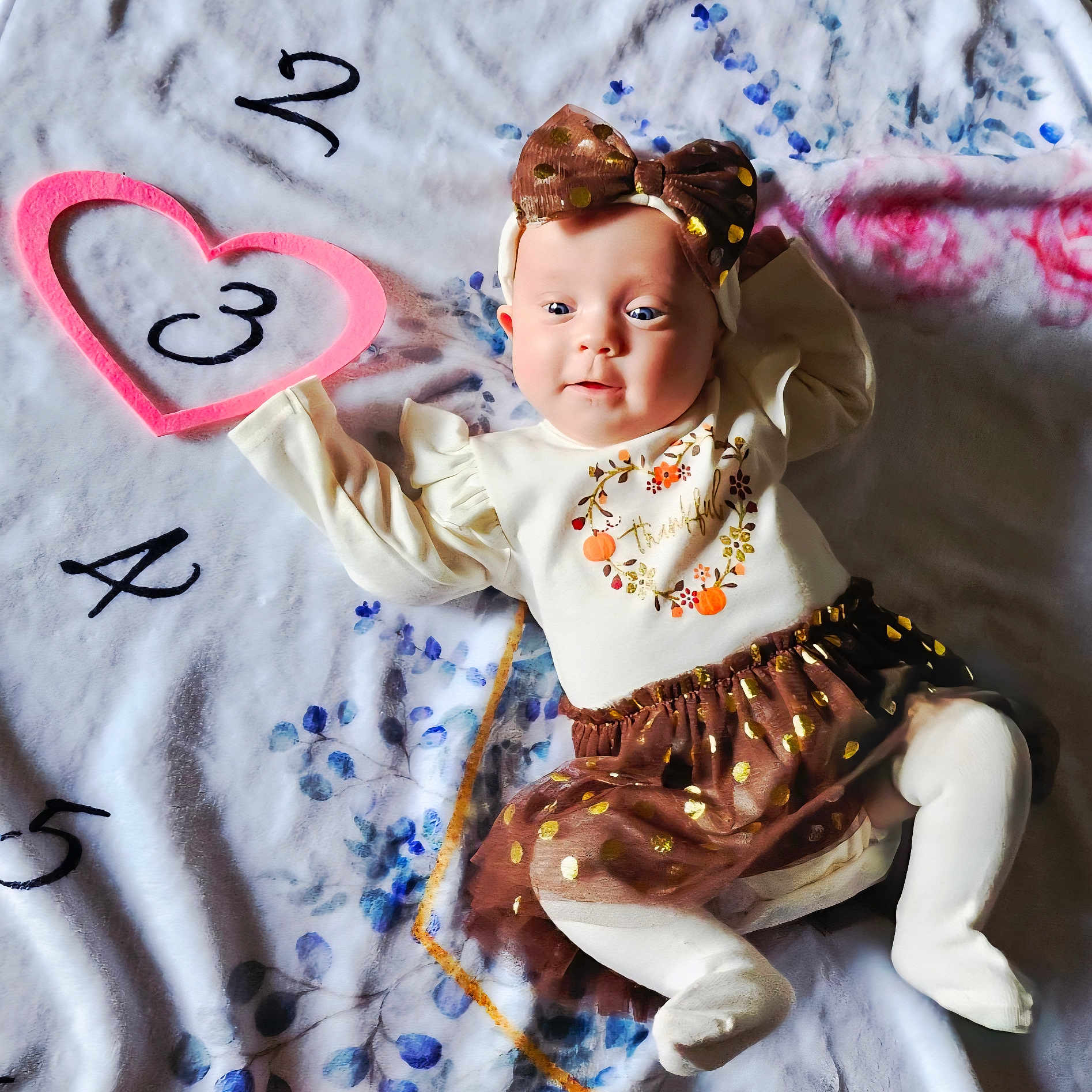 Layla is registered to the contest to win money with this photo: baby, blanket, bow, child, clothing, cute, festive, happy, headband, heart, indoors, infant, laying_down, numbers, pattern, portrait, skirt, smiling, soft_texture, tights