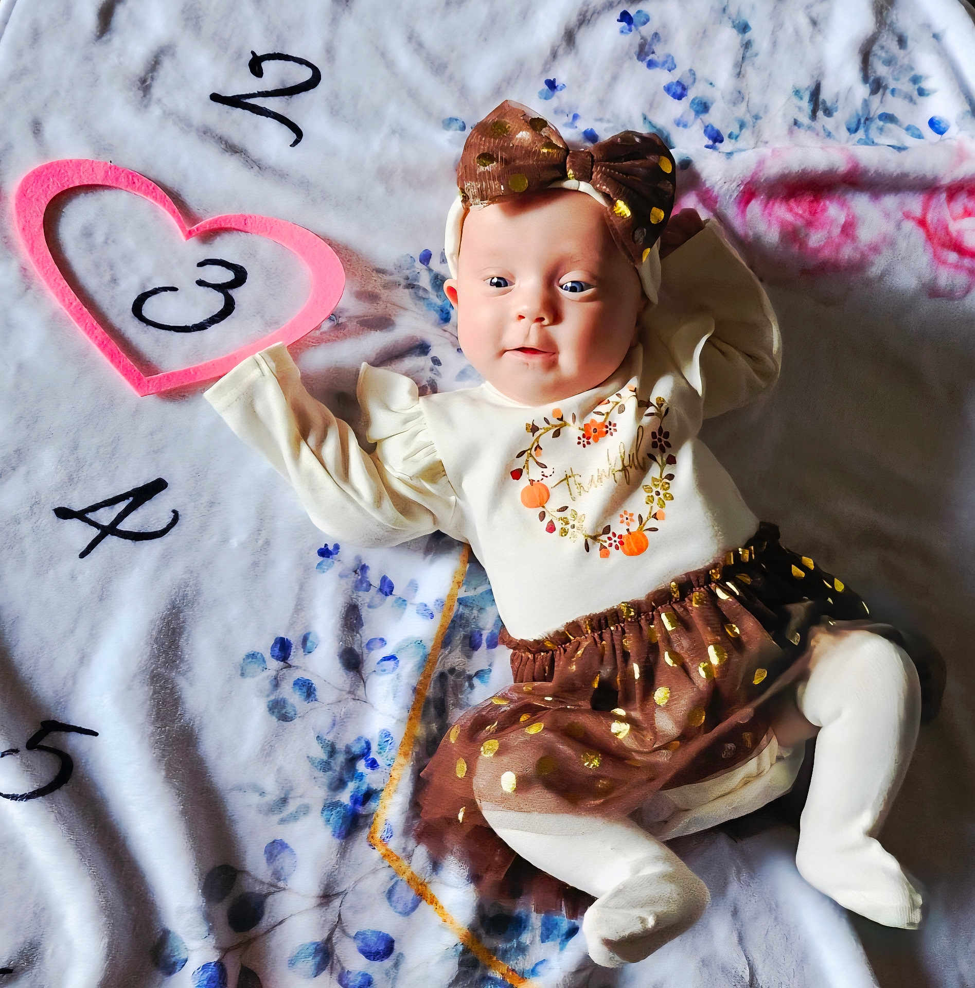 Layla is registered to the contest to win money with this photo: baby, infant, child, blanket, headband, bow, cute, smiling, laying_down, clothing, tights, skirt, pattern, numbers, heart, soft_texture, indoors, portrait, happy, festive