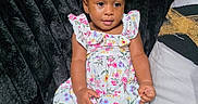 Mariah joined the competition — help win amazing prizes! baby, black_couch, bow, child, comfortable, couch, curly_hair, cute, fashion, floral_dress, girl, indoor, person, plush, portrait, sitting, smiling, toddler, white_shoes, young_child