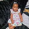baby, black_couch, bow, child, comfortable, couch, curly_hair, cute, fashion, floral_dress, girl, indoor, person, plush, portrait, sitting, smiling, toddler, white_shoes, young_child
