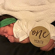 Estella joined the competition — help win amazing prizes! baby, sleeping, infant, headband, white_clothing, blanket, wooden_sign, one_month, newborn, cute, peaceful, indoors, portrait, child, resting, hand, face, soft_texture, black_surface, milestone