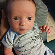 Ashton is registered to the contest to win money with this photo: baby, newborn, infant, onesie, blue_eyes, face, head, hand, arm, skin, hair, sitting, looking_at_camera, portrait, indoor, fabric, chair, tile_floor, cozy, adorable