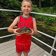 Illia joined the competition — help win amazing prizes! child, turtle, wildlife, outdoor, forest, pond, bridge, wooden_deck, portrait, smiling, standing, red_clothing, sportswear, basketball_jersey, shorts, nature, greenery, water, animal, railings