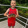 child, turtle, wildlife, outdoor, forest, pond, bridge, wooden_deck, portrait, smiling, standing, red_clothing, sportswear, basketball_jersey, shorts, nature, greenery, water, animal, railings
