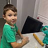 child, boy, baking, cookies, dough, rolling_pin, kitchen, table, flour, homemade, cooking, smiling, portrait, indoors, green_shirt, pants, chair, window, blinds, food