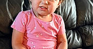 Emilia And Olivia is registered to the contest to win money with this photo: child, toddler, portrait, curly_hair, smiling, serious_expression, pink_clothing, floral_pattern, purple_toy, sitting, couch, black_leather, indoor, home, close_up, face, arms, legs, playtime, photography