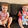 children, toddlers, siblings, girls, sitting, couch, indoor, portrait, faces, curly_hair, smiling, pouting, remote_control, stuffed_animal, doll, toys, pink_clothing, leather_couch, family, home