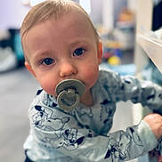 Enzo participe au concours pour gagner de l'argent avec cette photo : baby, blue_eyes, blurred_background, child, cute, face, furniture, home, indoor, infant, leaning, onesie, pacifier, person, playroom, portrait, smiling, soft_lighting, toy, young_child