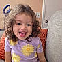Kilanna joined the competition — help win amazing prizes! toddler, child, curly_hair, purple_clothing, yellow_flowers, smiling, tongue_out, sitting, couch, orange_pillow, indoor, playful, happy, young_child, cute, person, home, furniture, portrait, casual