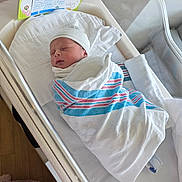 Caleb is registered to the contest to win money with this photo: newborn, baby, hospital, bassinet, blanket, swaddled, sleeping, bottle, card, hat, infant, bed, white, striped, person, healthcare, care, cute, rest, wrapped