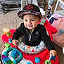 Mkilye is registered to the contest to win money with this photo: toddler, child, baby_walker, toy, cap, hat, black_jacket, smile, happy, indoor, carpet, colorful, playtime, person, hand, face, headwear, furniture, living_room, cute