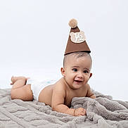 Felipe is registered to the contest to win money with this photo: baby, infant, diaper, blanket, hat, party_hat, smiling, cute, lying_down, soft_texture, celebration, portrait, child, adorable, young, happy, skin, headwear, pom_pom, studio