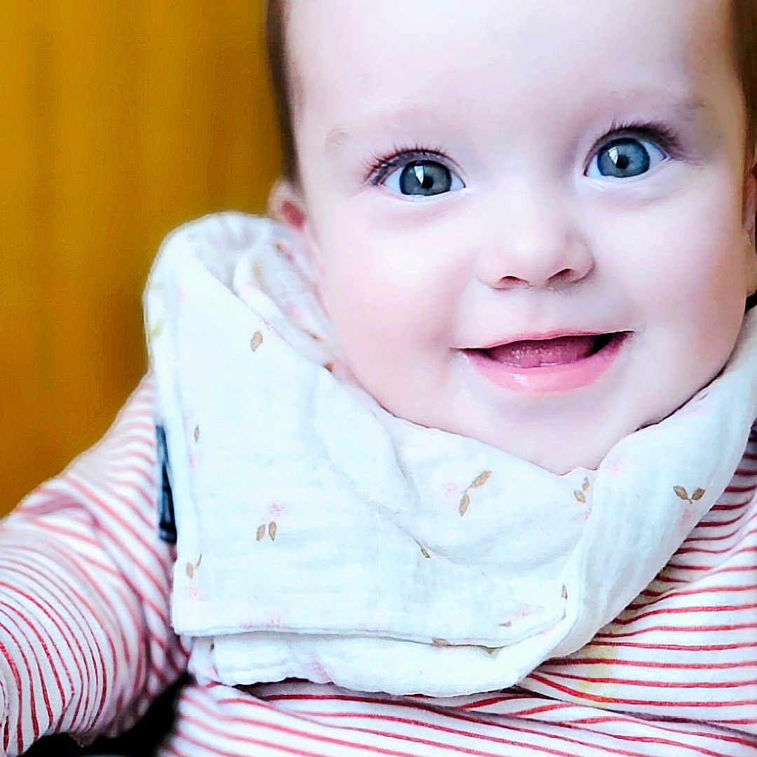 Margot participe au concours pour gagner de l'argent avec cette photo : baby, baby_carrier, bib, blue_eyes, child, close_up, clothing, cute, face, happy, indoor, infant, person, portrait, seated, smile, soft_lighting, striped_shirt, yellow_background, young_child