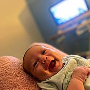 Kaïs participe au concours pour gagner de l'argent avec cette photo : baby, smiling, infant, blanket, pink, lying_down, happy, face, indoors, television, blurred_background, toddler, cute, child, soft_texture, clothing, portrait, skin, hand, expression