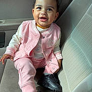 Kaylani joined the competition — help win amazing prizes! toddler, child, smiling, sitting, car_seat, pink_clothing, black_shoes, curly_hair, hair_bow, jacket, pants, happy, person, casual_wear, interior, car, seat, footwear, portrait, cute