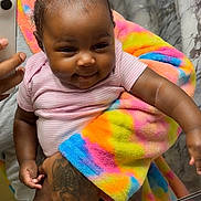 Rivyr is registered to the contest to win money with this photo: adult_hand, baby, bathroom, bow, child, close_up, colorful, hair_bow, happy, indoor, infant, mirror, mirror_selfie, pink_shirt, portrait, rainbow_blanket, seated, smartphone, smiling, tattoo