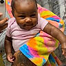adult_hand, baby, bathroom, bow, child, close_up, colorful, hair_bow, happy, indoor, infant, mirror, mirror_selfie, pink_shirt, portrait, rainbow_blanket, seated, smartphone, smiling, tattoo