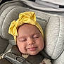 baby, smiling, headband, yellow_bow, car_seat, straps, closed_eyes, child, infant, cute, soft_lighting, face, happy, comfort, clothing, floral_pattern, seatbelt, portrait, indoors, sleepy