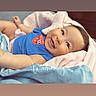baby, infant, smile, blue_shirt, strawberry_graphic, blanket, pink_blanket, cozy, lying_down, happy, cute, child, portrait, indoors, soft_lighting, warm_colors, face, skin, expression, clothing