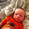 Silas Jericho Day is registered to the contest to win money with this photo: baby, infant, orange_shirt, cartoon_character, blanket, bed, expression, face, clothing, person, portrait, indoors, resting, cute, young_child, skin, hair, lying_down, closeup, toddler
