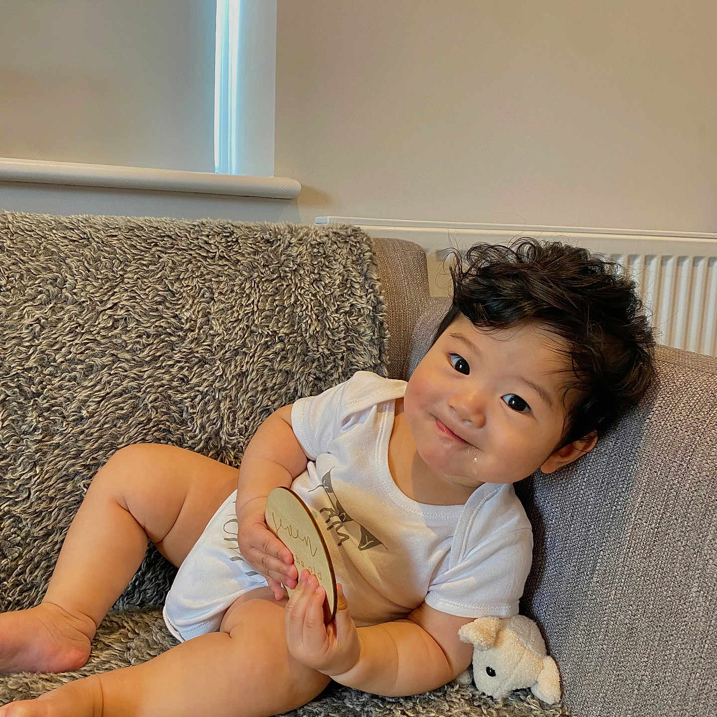 Caleb is registered to the contest to win money with this photo: baby, child, chubby, couch, cozy, curly_hair, cute, happy, home, indoors, infant, milestone_plaque, plush_toy, portrait, relaxing, smile, sofa, soft_light, texture, white_onesie