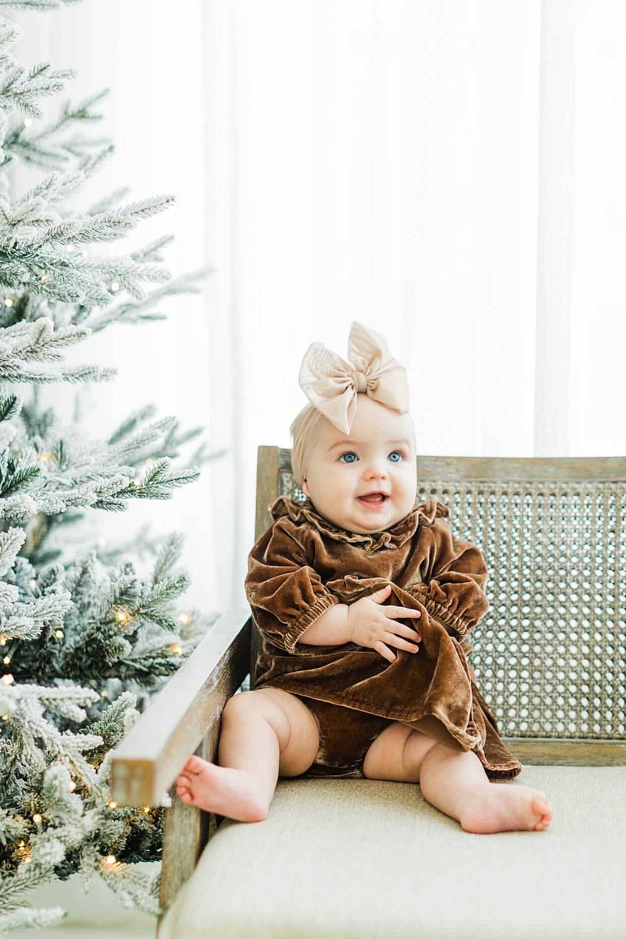 Elise is registered to the contest to win money with this photo: baby, baby_toddler_clothing, brown_hair, cap, child, christmas_tree, doll, dress, event, fawn, foot, fur, human_body, jewellery, ornament, person, sitting, sleeve, teddy_bear, toy