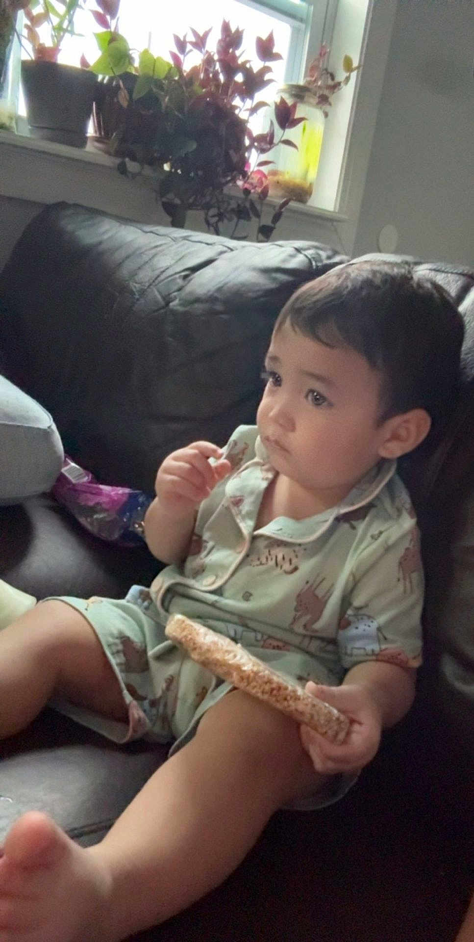 Yonathan joined the competition — help win amazing prizes! toddler, child, pajamas, snack, rice_cake, couch, leather, indoor, window, plants, home, relaxed, sitting, cute, face, person, food, leisure, comfort, young_child