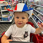 Dakota is registered to the contest to win money with this photo: aisle, boy, child, clothing, colorful, cowboy_hat, curious, cute, face, floor, indoor, person, products, retail, shelf, shopping, shopping_cart, store, toddler, white_tshirt