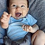 baby, infant, smiling, happy, blue_clothing, plush_seat, soft_texture, cute, child, young, indoors, seated, playful, chubby_legs, hand_gesture, bright_eyes, joyful, comfort, casual, portrait
