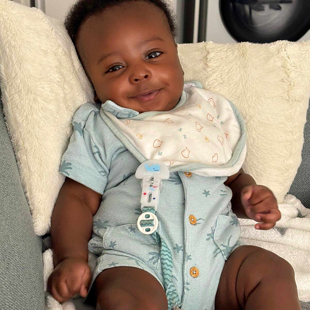 Chris-Owen a rejoint le concours — aidez-le/la à gagner de superbes lots ! baby, bib, blanket, child, clothing, cozy, cushion, cute, face, furniture, happy, indoor, infant, pacifier, person, portrait, relaxed, sitting, skin, smiling