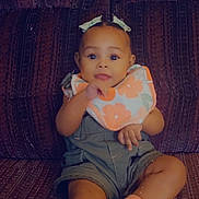 Kayomi is registered to the contest to win money with this photo: baby, child, couch, bib, denim_overalls, socks, bows, face, smile, indoor, seated, person, cute, patterned_fabric, infant, happy, portrait, relaxed, clothing, skin