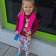Nova is registered to the contest to win money with this photo: child, girl, backpack, smile, sidewalk, window, reflection, floral_leggings, sneakers, casual_clothing, outdoor, daylight, happy, cute, standing, concrete, urban, playful, young, portrait