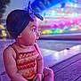Ayla a rejoint le concours — aidez-le/la à gagner de superbes lots ! blue_light, blurred_background, casual_clothing, child, colorful, curious, cute, headband, neon_lights, night, orange_top, outdoor, patterned_clothing, purple_light, side_profile, sitting, soft_lighting, toddler, wooden_floor, young_child