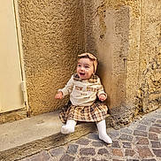 Ayla participe au concours pour gagner de l'argent avec cette photo : baby, building, child, clothing, cobblestone, daylight, girl, happy, headband, outdoor, person, plaid_skirt, portrait, sitting, smiling, street, texture, urban, wall, white_tights