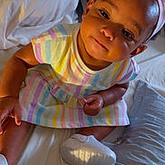 Haven is registered to the contest to win money with this photo: baby, child, infant, girl, headband, pink_bow, striped_dress, bed, pillow, white_shoes, sitting, indoors, cute, portrait, smiling, person, soft_lighting, closeup, happy, young_child