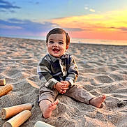 Jules participe au concours pour gagner de l'argent avec cette photo : toddler, child, beach, sand, sunset, smile, happy, barefoot, wooden_pieces, toy, outdoor, nature, sky, clouds, playing, sitting, casual_clothing, portrait, sunlight, fun