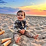 toddler, child, beach, sand, sunset, smile, happy, barefoot, wooden_pieces, toy, outdoor, nature, sky, clouds, playing, sitting, casual_clothing, portrait, sunlight, fun