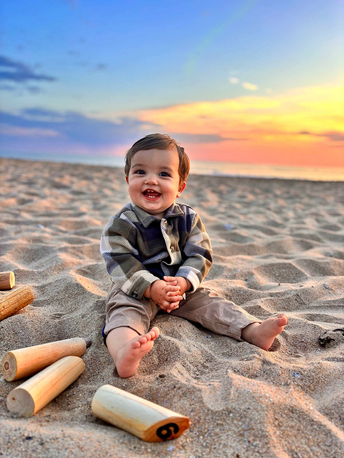 Jules participe au concours pour gagner de l'argent avec cette photo : toddler, child, beach, sand, sunset, smile, happy, barefoot, wooden_pieces, toy, outdoor, nature, sky, clouds, playing, sitting, casual_clothing, portrait, sunlight, fun
