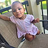 child, toddler, baby, portrait, smiling, seated, dress, striped_clothing, pink, chair, outdoor, patio, furniture, face, eyes, earrings, barefoot, relaxed, candid, photography