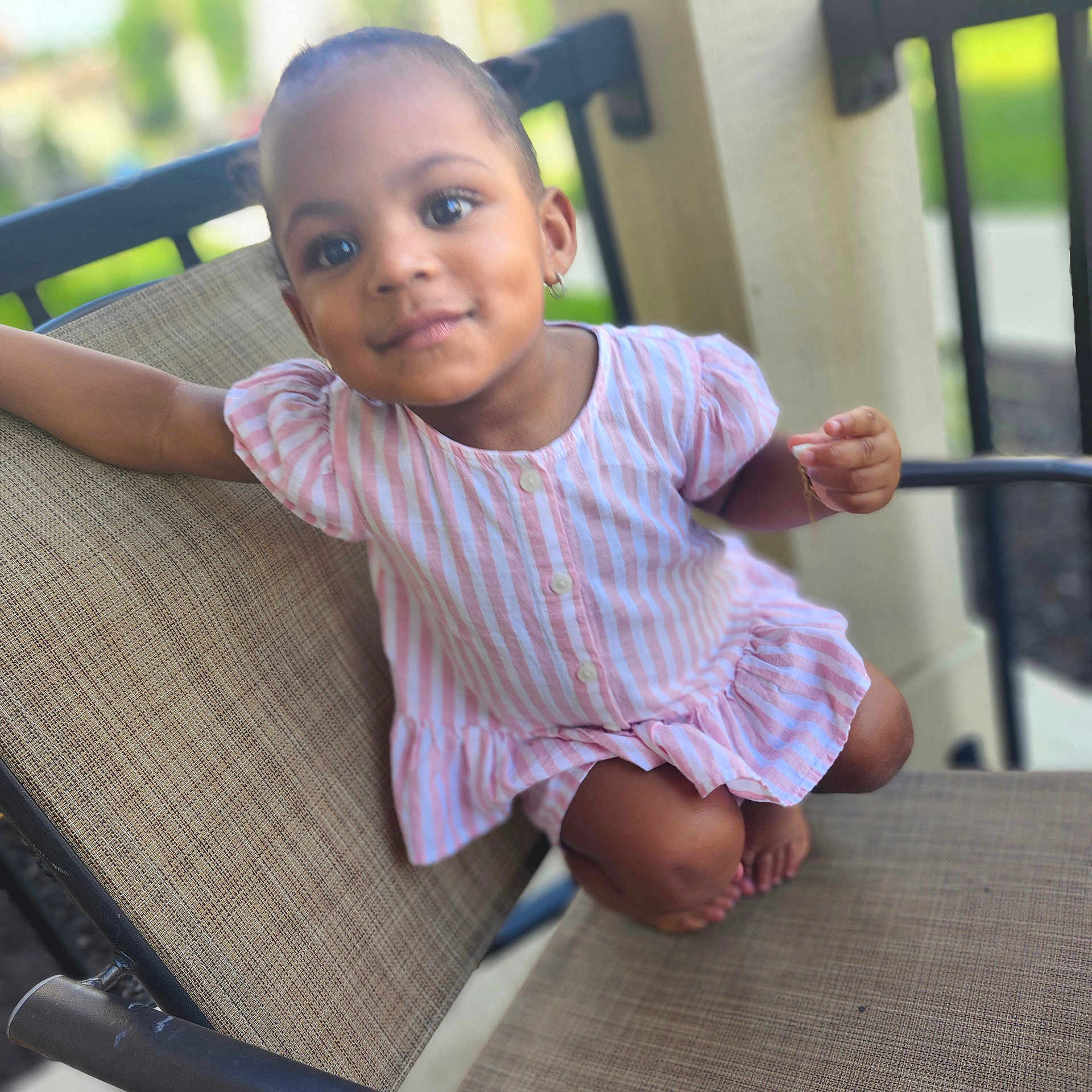 Nashkiely joined the competition — help win amazing prizes! child, toddler, baby, portrait, smiling, seated, dress, striped_clothing, pink, chair, outdoor, patio, furniture, face, eyes, earrings, barefoot, relaxed, candid, photography