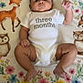 baby, infant, three_months, onesie, blanket, floral_pattern, fox, owl, cute, chubby, child, lying_down, raised_fist, curious, indoors, soft_texture, colorful, adorable, newborn, portrait