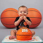 Zaiden joined the competition — help win amazing prizes! baby, cake, birthday, basketball, celebration, smiling, orange, frosting, hands, face, sitting, toy, happy, child, foot, black_shirt, bracelet, table, indoor, photography
