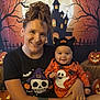 woman, baby, halloween, costume, smile, pumpkin, jack_o_lantern, haunted_house, spooky, background, tattoo, black_shirt, orange_outfit, hat, festive, holiday, face, portrait, indoor, family
