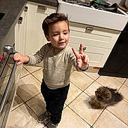 Dinis a rejoint le concours — aidez-le/la à gagner de superbes lots ! black_pants, boy, cabinet, child, dish_rack, dog, fluffy_dog, gray_shoes, indoor, kitchen, kitchen_counter, oven, peace_sign, sink, small_dog, smiling, standing, sweater, tile_floor, utensils