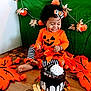 toddler, child, halloween, orange_clothing, pumpkin, decorations, striped_leggings, cake, chocolate_cake, whipped_cream, floor, leaf_cutouts, smiling, curly_hair, headband, festive, indoor, celebration, holiday, happy
