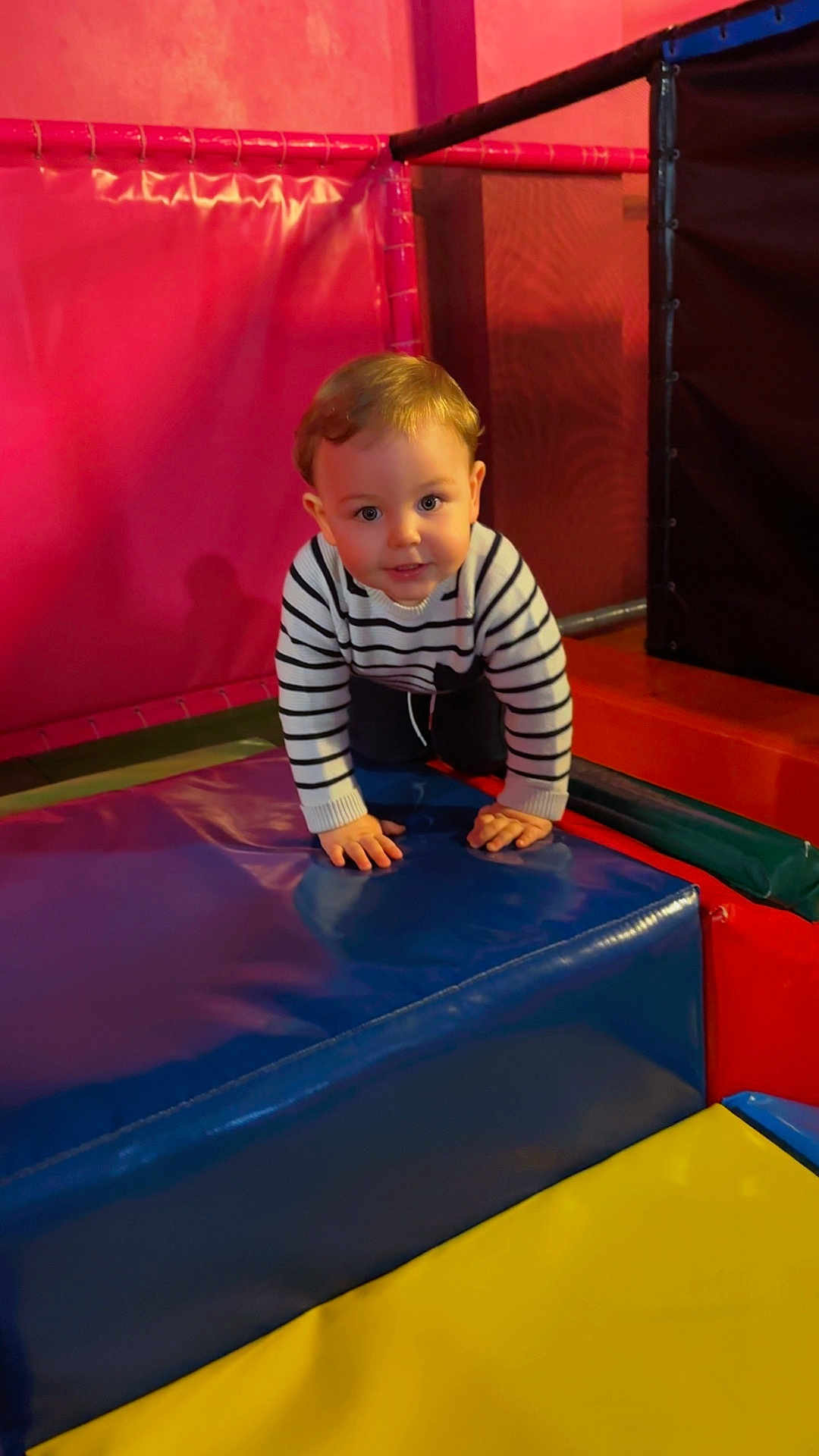 Conor participe au concours pour gagner de l'argent avec cette photo : child, baby, toddler, crawling, play_area, padded_mat, foam_block, striped_sweater, hands, eyes, hair, smile, indoor, playground, colorful, blue, pink, yellow, soft_play, portrait