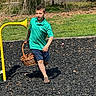 activity, basket, boy, casual_clothing, child, daylight, fun, grass, green_shirt, nature, outdoor, park, playground, running, sand, shorts, summer, toy, tree, yellow