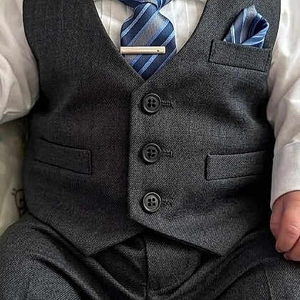 Legend is registered to the contest to win money with this photo: baby, child, suit, tie, vest, formal_wear, shoes, infant, portrait, serious_expression, seated, indoors, cushion, patterned_background, person, young_child, fashion, clothing, cute, small
