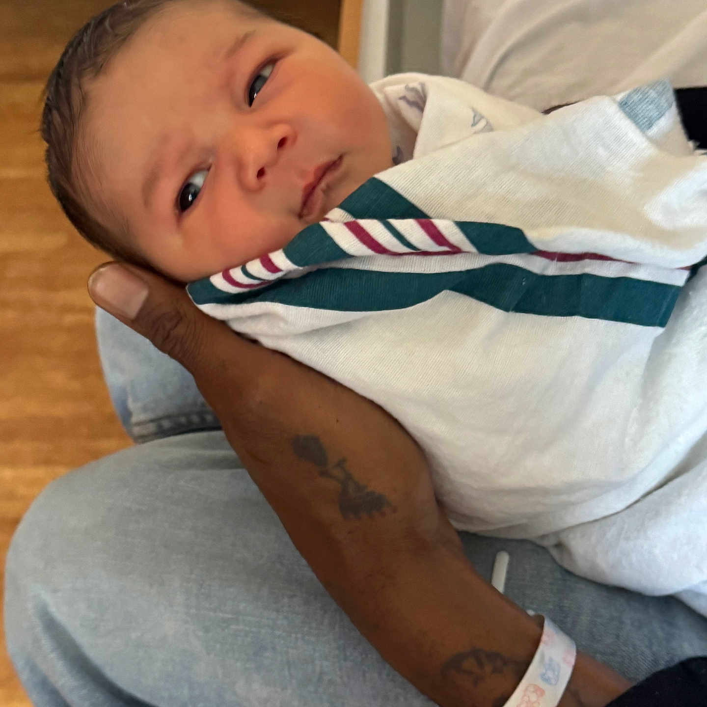 Legend is registered to the contest to win money with this photo: newborn, baby, infant, wrapped, blanket, hospital, hand, tattoo, wristband, person, clothing, face, skin, holding, seated, indoor, curious, young, portrait, cozy