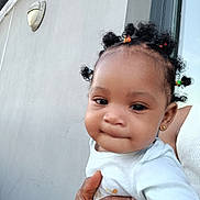 Mariam Sarr participe au concours pour gagner de l'argent avec cette photo : baby, child, curly_hair, cute, earrings, expression, face, hair_buns, hand, holding, human, infant, light, outdoor, person, portrait, skin, wall, white_shirt, young